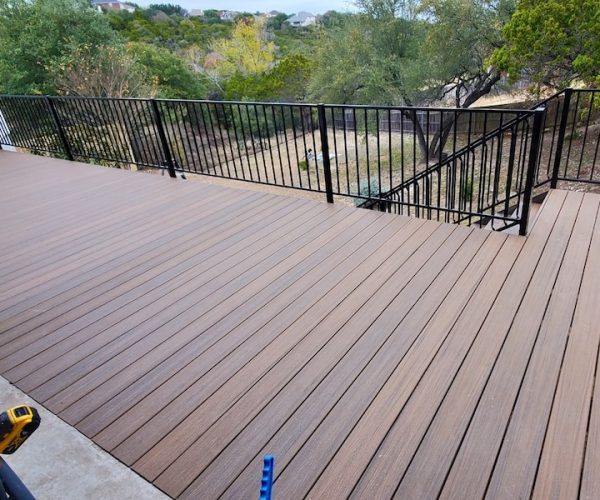 spacious wooden deck with parallel planks and a sleek black metal railing overlooks a lush green backyard, creating a serene, inviting atmosphere.