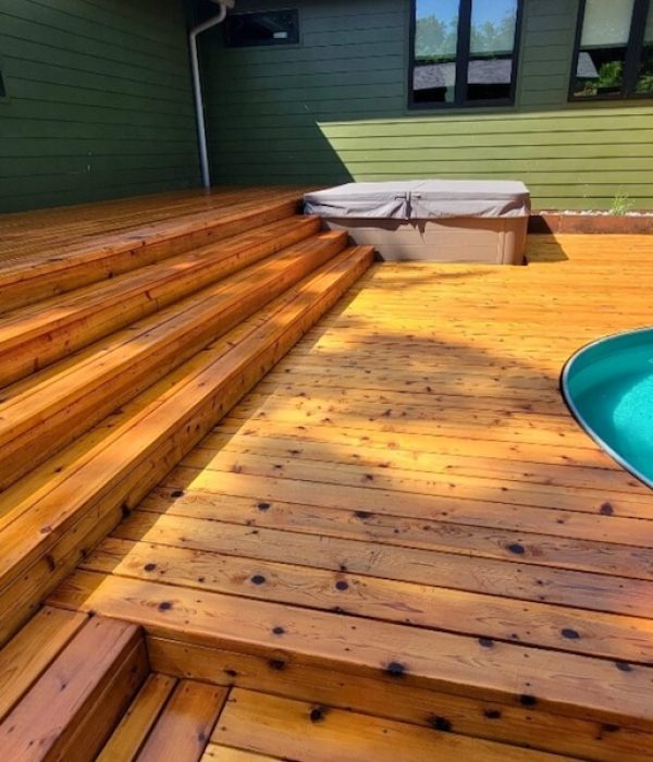 Sunlit wooden deck with steps leading to a jacuzzi and a circular hot tub. The vibrant wood contrasts with the aqua blue water, creating a serene ambiance.