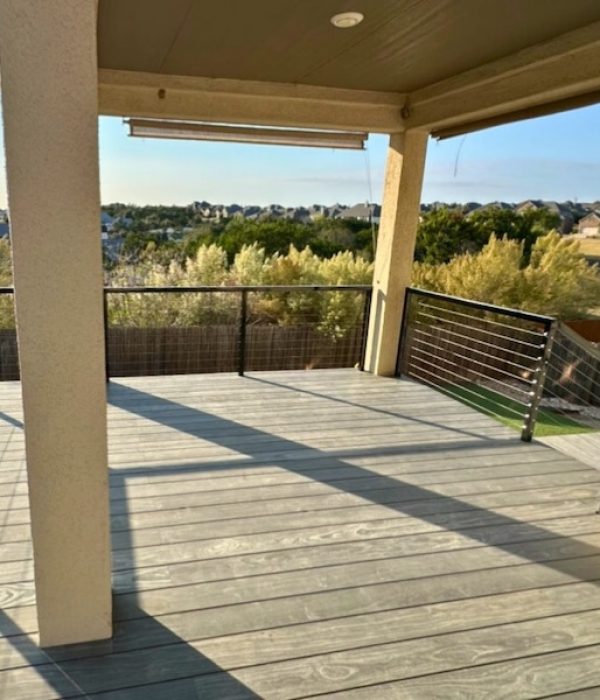 Sunny wooden deck with metal railing, shaded by an overhanging roof. Overlooks suburban houses and trees, creating a serene and open atmosphere.